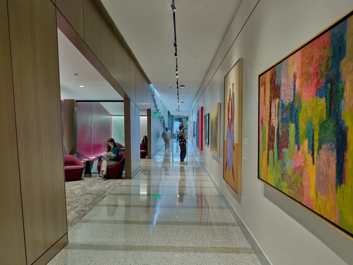 People look at art hanging on the wall of a long hallway